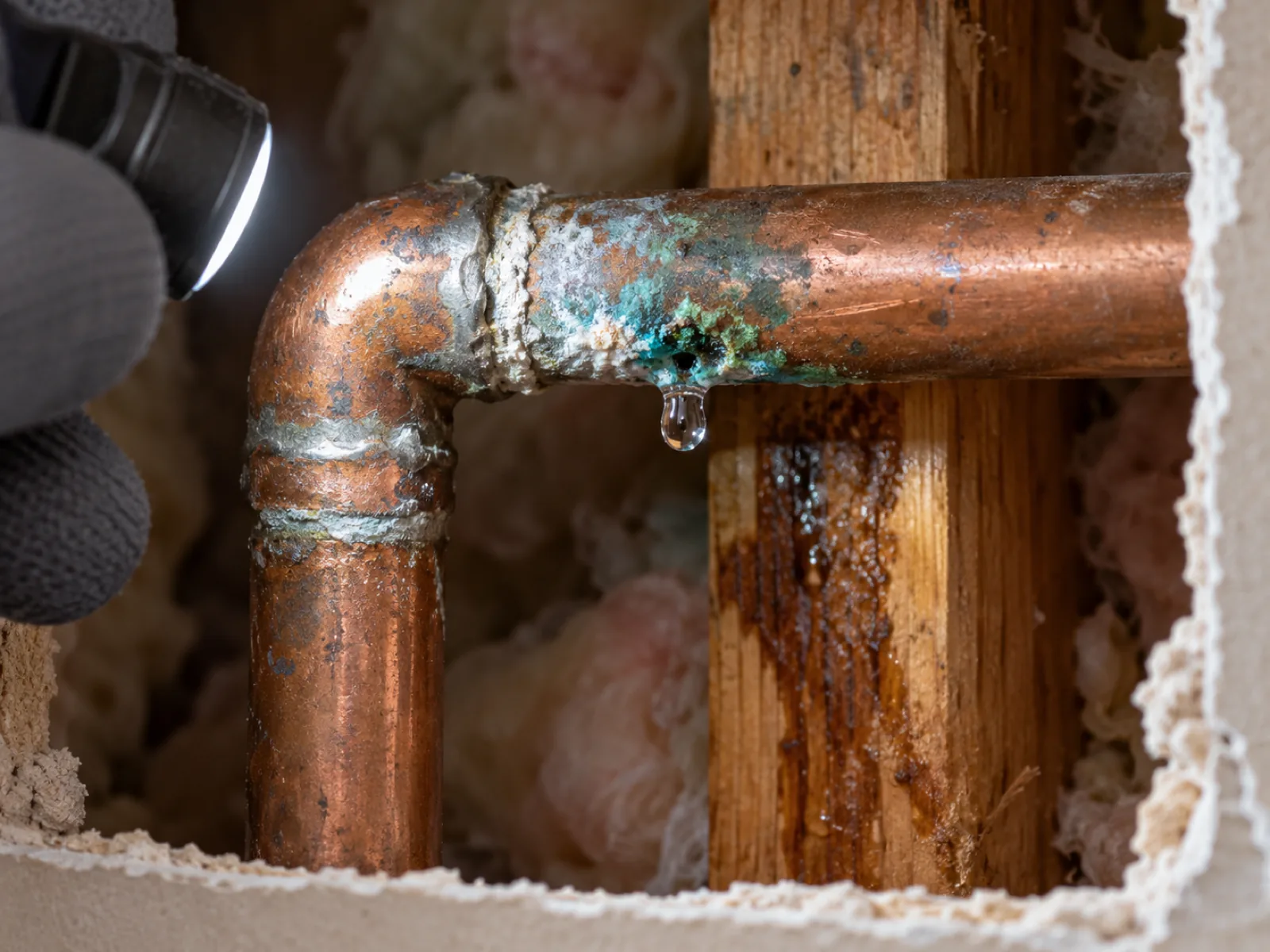 Water droplet forming at a pinhole on a green-stained copper pipe joint inside an opened wall in Las Vegas, NV